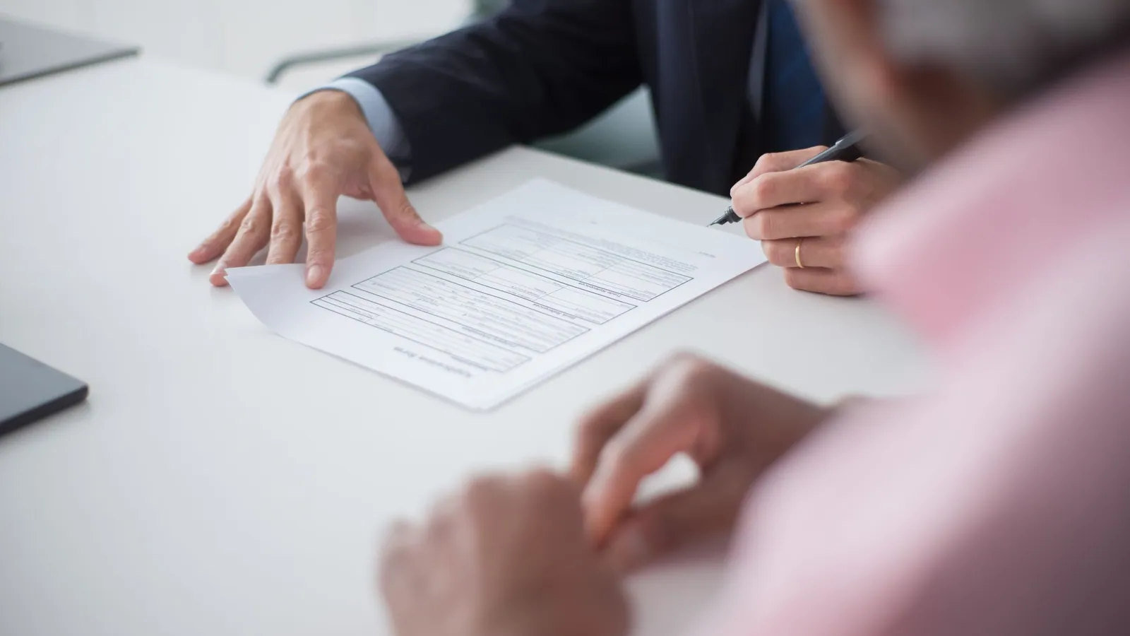 A professional completing a form at a white desk while a colleague looks on