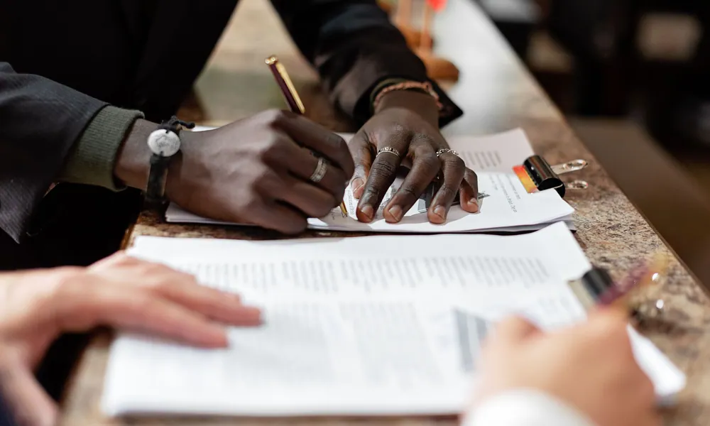 Close view of hands signing a document at a counter while a second file is reviewed in the foreground